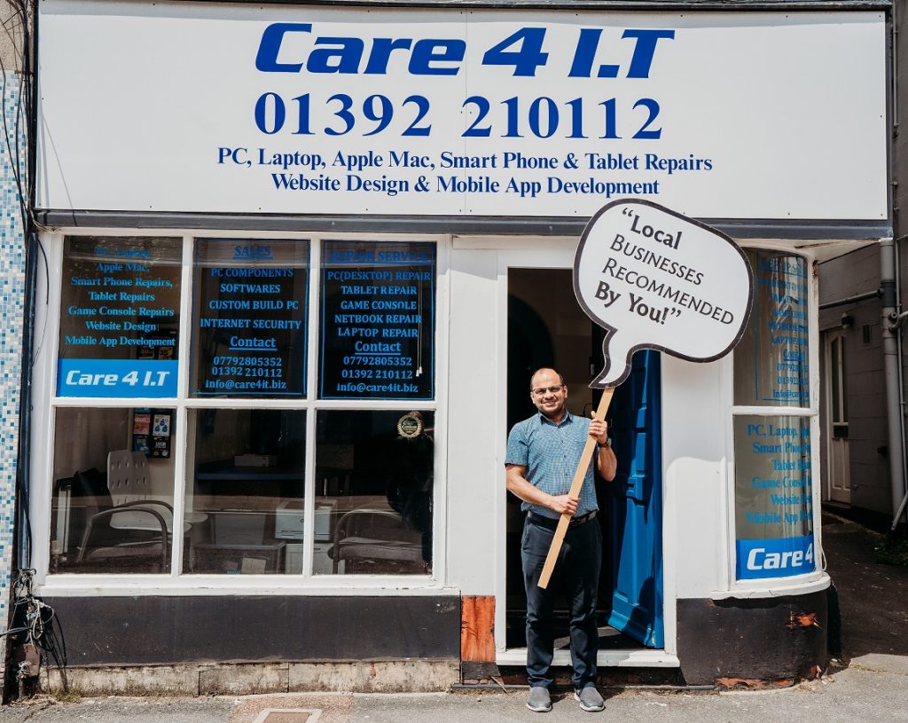 Man standing outside Computer Repair Shop holding sign 'local businesses recommended by you'
